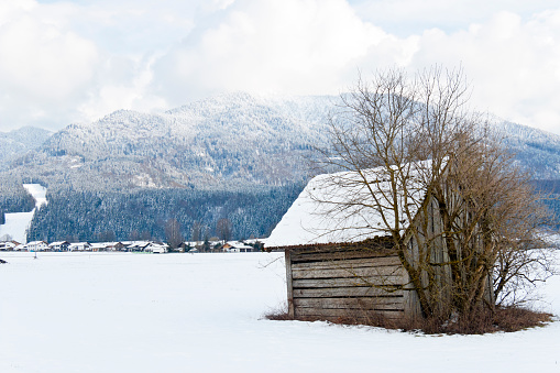 Old barn and snowcapped mountains surrounded with snow clouds in the Bavarian Alps, Germany.