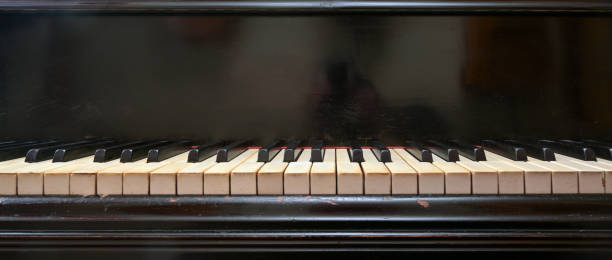 Old black grand piano keyboard with keys from ivory and ebony, part of a musical instrument in panoramic format, copy space, selected focus, narrow depth of field stock photo