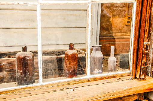 A group of bottles were left on a window sill in an abandoned ghost town.