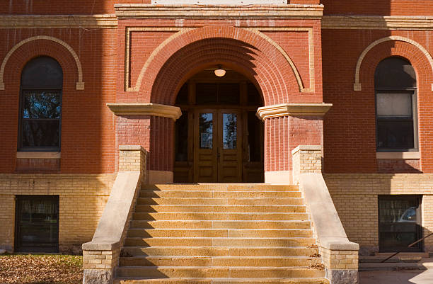 Old Brick School Building Exterior Front Entrance Door and Steps Horizontal straight-on exterior view of an old red brick high school or elementary schoolhouse building facade, centered on the entrance front door and staircase.  The traditional architecture suggests a respect for higher education and learning. The brownstone built structure is located in a small Midwestern town in the U.S.A. school exteriors stock pictures, royalty-free photos & images