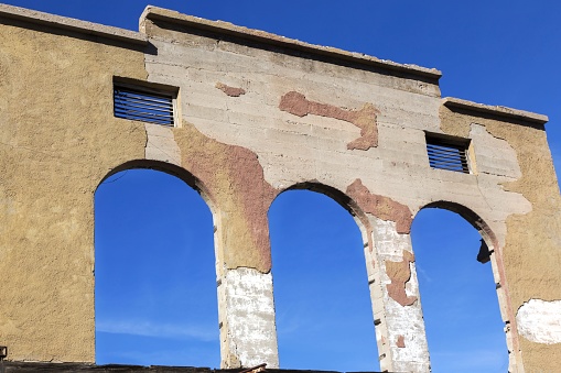 Old Grocery Store Ruin Exterior with Crumbling Facade Arch in Front of Art Studio against Blue Sky Background in Jerome Arizona City Main Street