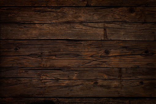 Old weathered dark wooden table board. Wood knots, cracks, stains, scratches and other damages are strongly expressed. All planks have a strong clear texture of wood. A wood grain pattern featuring even grains of wood running horizontally across the image. Compounds of the planks are clearly visible.