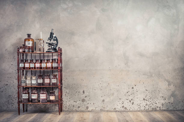 Old laboratory bottles, antique microscope, vintage lab glassware support on the wooden shelving front concrete wall background. Retro style filtered photo stock photo