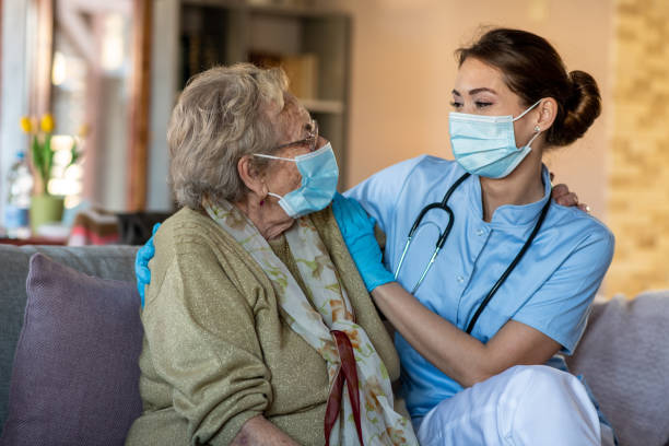 Old lady with care specialist, sitting and talking with face masks on. stock photo