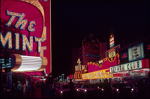 Las Vegas, Nevada, USA, 1968. The Freemont Street in old Las Vegas at night. To the left, the entrance to the Mint Casino. Furthermore, illuminated advertising, visitors and traffic.