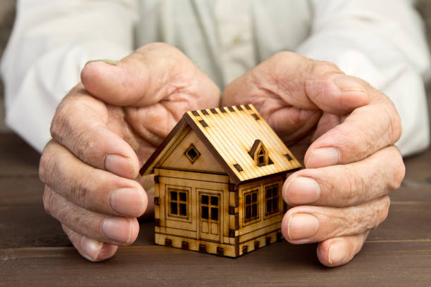 Old man protecting house model with hands.Risk insurance.The concept of mortgages and Bank loans. Poverty. Rental property. stock photo