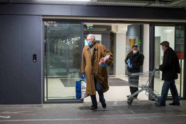 Old man wearing protective medical mask and gloves leaving grocery shopping store and carrying groceries. Panic buying during coronavirus senior shopping hours. Coronavirus lockdown. stock photo