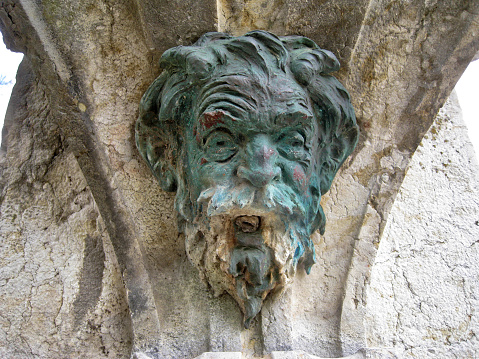 Detail of an old Bronze statue water source with a face of an old men. Photo taken of a portuguese park in Lisbonne - Portugal called \