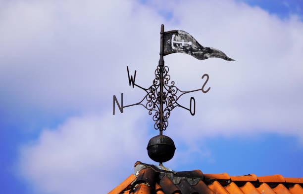 Old metal weather vane on the roof of a building with the four cardinal points. Blue sky in the background. stock photo