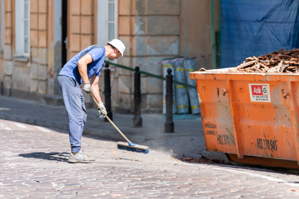 Old or new town street with man worker cleaner in blue uniform cleaning trash dust from cobblestone cobbled road by dumpster and sweeper tool during day stock photo