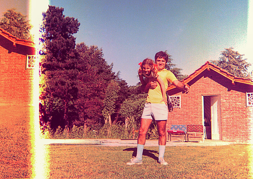 Vintage and damaged photo of a girl and her father playing outdoors