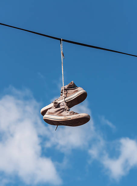old sneakers on a wire old sneakers (shoes) on a wire telephone line stock pictures, royalty-free photos & images