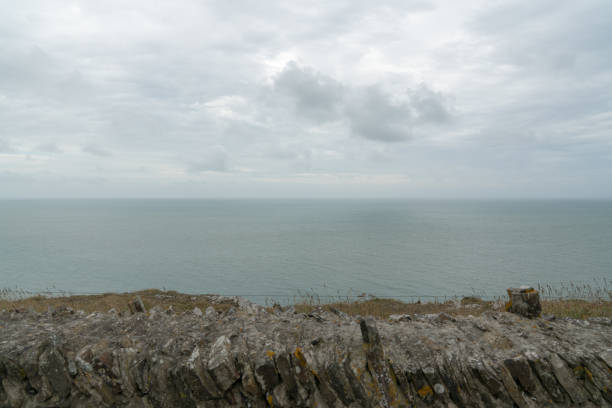 old stone rock wall and view over an expanisve ocean under an overcast sky An old stone rock wall and view over an expanisve ocean under an overcast sky barneville carteret photos stock pictures, royalty-free photos & images