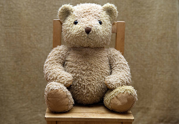 Old teddy bear sitting on wooden chair stock photo