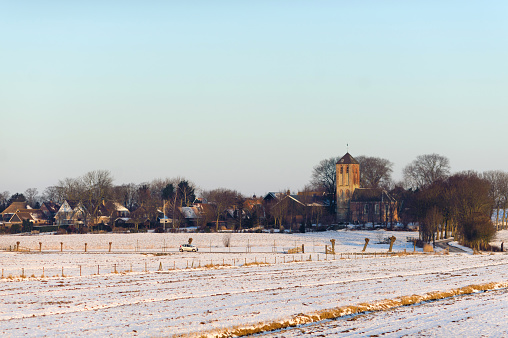 Old traditional church and fields in snow in Hippolytushoef at winter, North Holland, Netherlands.
