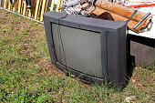 istock Old TV set dumped and left in the garden along with other bulky trash. Old TV thrown away next to a wall with a pile of mixed garbage in natural environment. Recycling industry. Not Ecology. Ecology. 872156750