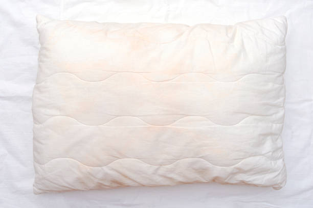 Old used white pillow with stains on crumpled sheet, dirty pillow on the bed stock photo