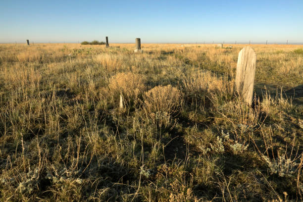 Slowly decaying along the road a weathered wooden grave maker and tombstone headstones of the Sligo Cemetery are slowly consumed by the prairie in the Pawnee National Grasslands in northern Colorado.