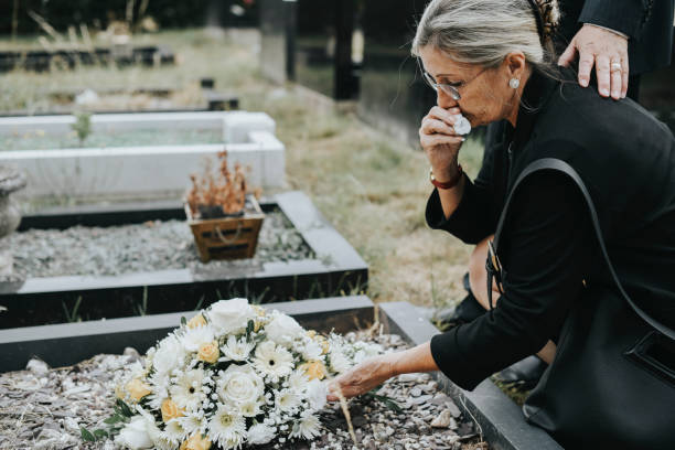 Old woman laying flowers on a grave stock photo