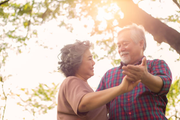 Old woman or wife dancing with old man or husband at park under tree in morning. Grandmother and grandfather feel happiness at the wonderful moment time with smiley faces. Senior couple is romantic Senior couple Old woman or wife dancing with old man or husband at park under tree in morning. stock pictures, royalty-free photos & images