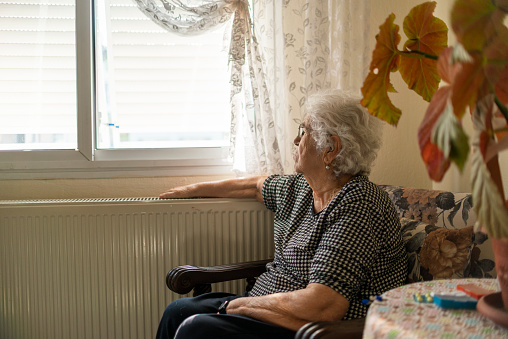 Old woman looking worried, sitting alone at home self isolating during coronavirus lockdown.