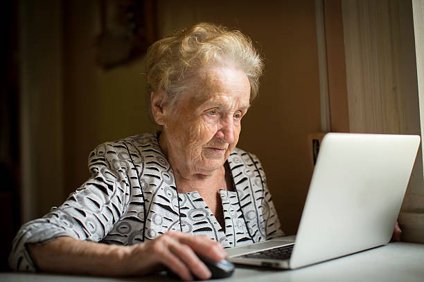 Old woman sitting with laptop at table in his house. stock photo