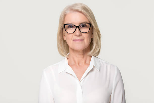 Older businesswoman in glasses looking at camera isolated on background Confident older businesswoman in glasses looking at camera, middle aged senior female professional, mature lady teacher business coach head shot portrait isolated on white grey studio background nurse face stock pictures, royalty-free photos & images