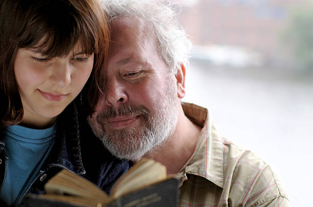 Older Father and Daughter Reading from Vintage Book Together stock photo