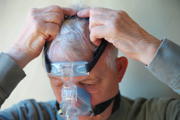 Older man puts on CPAP device head gear stock photo
