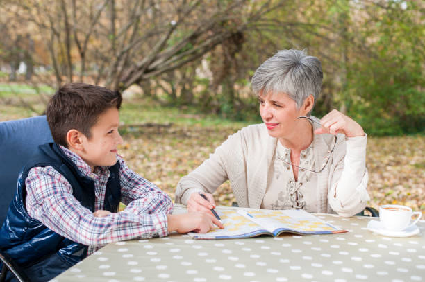 Older woman sitting with grandson and solves sudoku stock photo