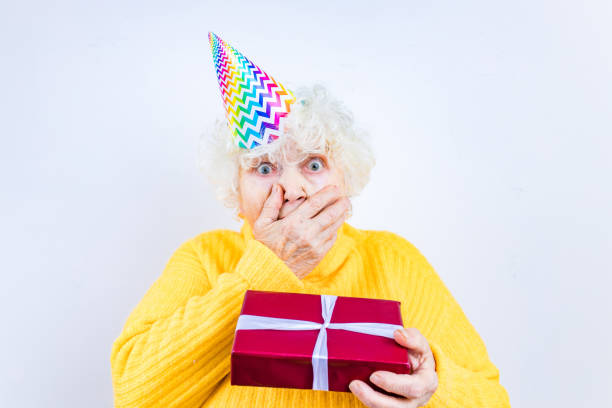 older woman with a gift wear yellow sweater and horn cap on a white background stock photo
