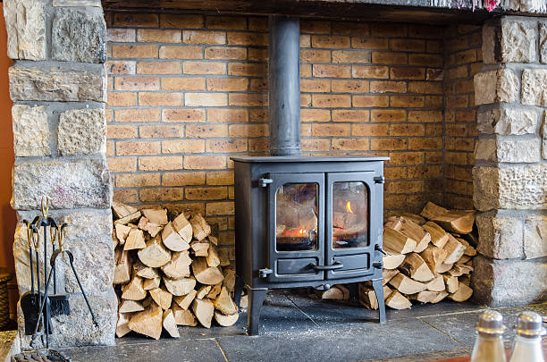 Old-fashioned Wood Burning Stove Tradional Wood Burning Stove in a Brick Fireplace. Two piles of firewood are placed at both sides of the stove and some fireplace accessories are visible at the left side of the photo. firewood stock pictures, royalty-free photos & images