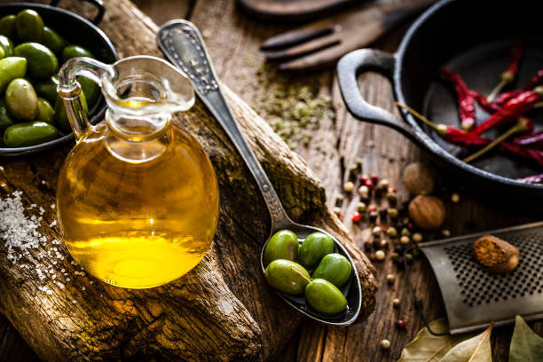 olive oil bottle and green olives shot on rustic wooden table - olive oil stock photos and pictures