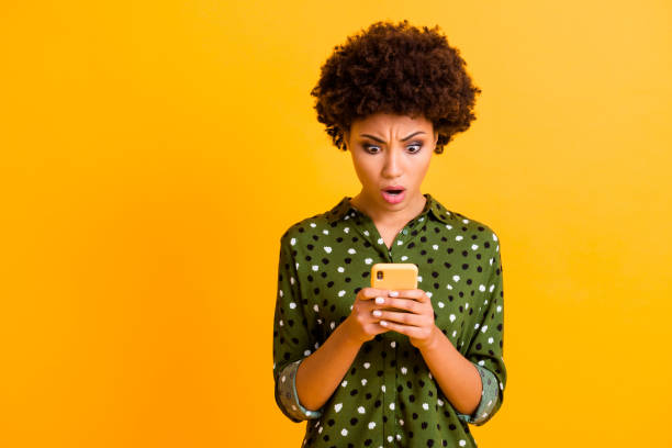 omg dess otroliga. förvånad galen afro amerikansk flicka använder smart telefon läsa sociala medier information få negativa reaktioner ogillar slitage snygga kläder isolerade glans färg bakgrund - omg girl bildbanksfoton och bilder