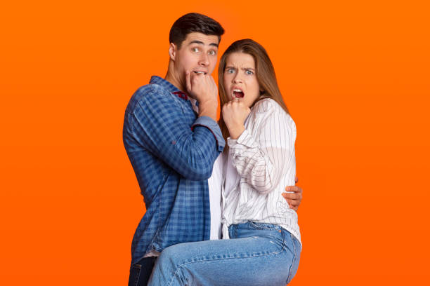Omg, what is this and portrait of scared couple, human emotions and facial expression Omg, what is this and portrait of scared couple, human emotions and facial expression. Young afraid, shocked, surprised and amazed man and lady with hands on faces isolated on orange background worried man funny stock pictures, royalty-free photos & images