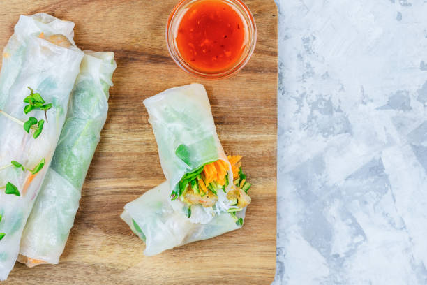 On a light background cutting board with spring roll. A healthy Asian snack with vegetables and shrimp. Photo with copy space. stock photo