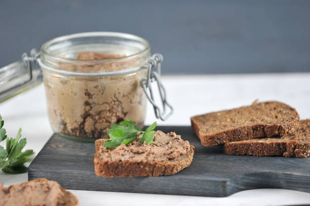 On a wooden board, several slices of black bread with liver pate. Next to a glass jar with pate. On a wooden board, several slices of black bread with liver pate. Next to a glass jar with pate. Close-up. liver pâté photos stock pictures, royalty-free photos & images