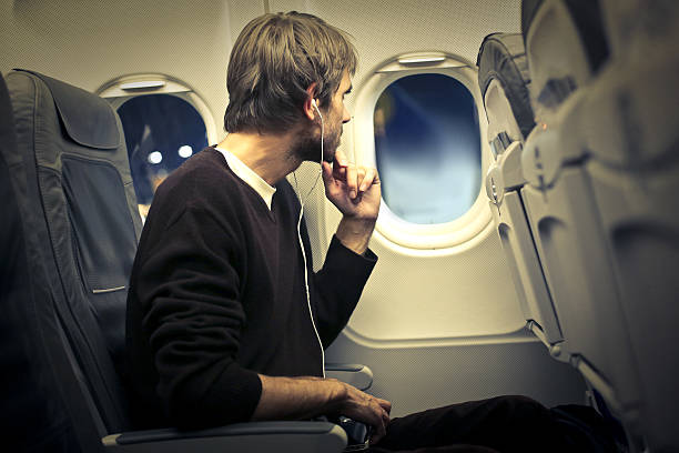 On the airplane A man is sitting in an airplane, looking out from a window, and looks really interested in hat he's seeing plane window seat stock pictures, royalty-free photos & images