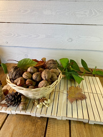 walnuts and hazelnuts lie in a basket on wooden pallets that lie on an oak table leaves visible in the background hay from pine boards painted white