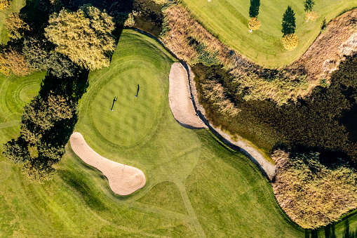 Drone perspective view of two golfers lining up their putts. They are in the beautiful surroundings of a golf course on the island of Moen in Denmark, surrounded by sand traps and water features. Horizontal format with some copy space.