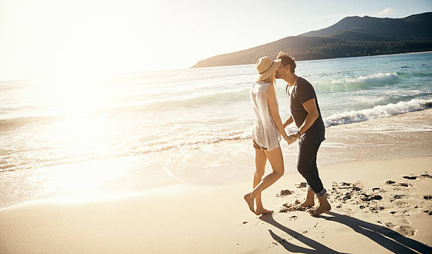 On vacation, you’re bound to get sun kissed Shot of a young couple enjoying a romantic kiss at the beach tasmania photos stock pictures, royalty-free photos & images