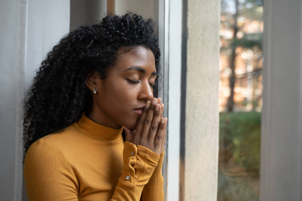 One black woman depressed in front of window prays stock photo