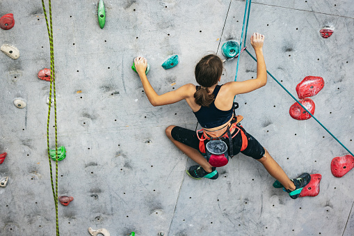 Little hiker. Portrait of active teen girl climbing the grey rock wall. Sport weekend action in adventure park. Active lifestyle concept