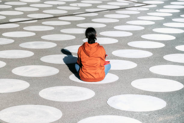 one girl in orange hoody sitting cross-legged on white spotted town square stock photo