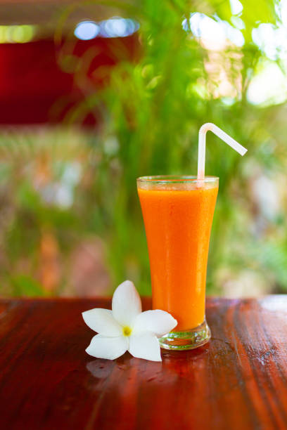 One glass with freshly squeezed juice and frangipani flower. One glass with freshly squeezed juice and frangipani flower. papaya smoothie stock pictures, royalty-free photos & images