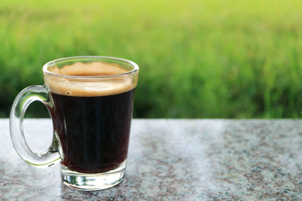 One Hot Black Coffee in a Transparent Glass with Blurry Green Meadow in Background One Hot Black Coffee in a Transparent Glass with Blurry Green Meadow in Background black coffee stock pictures, royalty-free photos & images