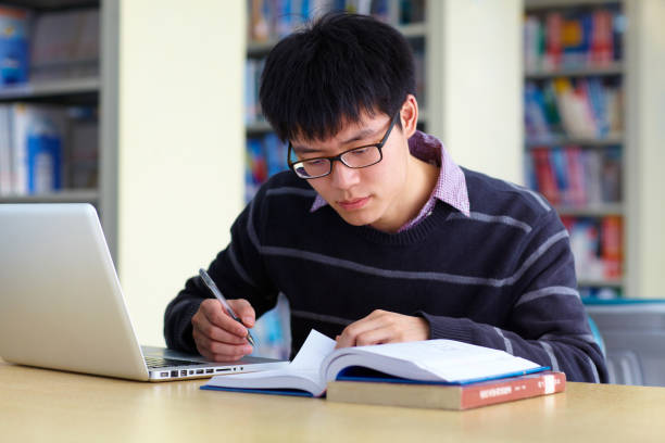 テーブルの上のノート パソコンを図書館で勉強する 1 つの男性のアジア大学生