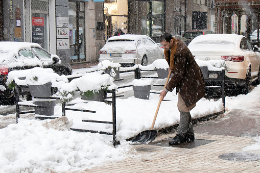 Belgrade, Serbia - January 11, 2022: One man using shovel for removing snow from city sidewalk in front of the coffee bar