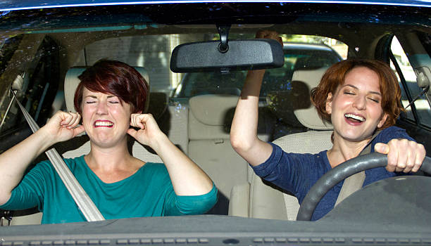 One woman singing and one woman covering her ears in a car stock photo