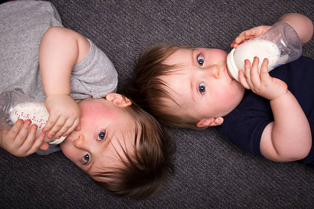 One year old twins drink from a bottle stock photo